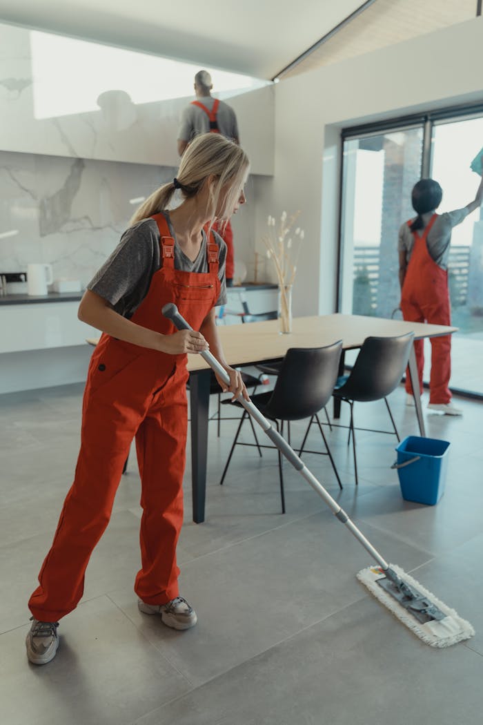 Cleaning team in red overalls mopping and sanitizing a modern home interior.